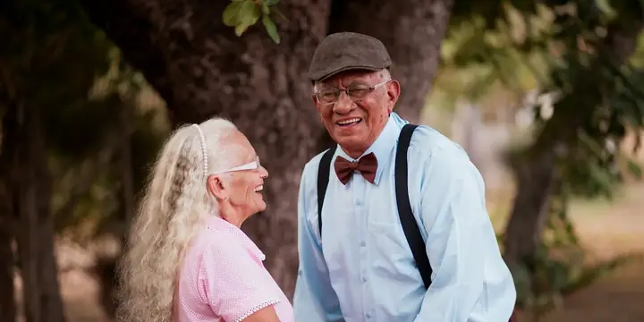 An older couple smiling and holding hands under the trees